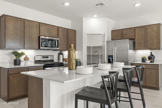 kitchen featuring a center island with sink, a kitchen bar, dark brown cabinetry, and appliances with stainless steel finishes