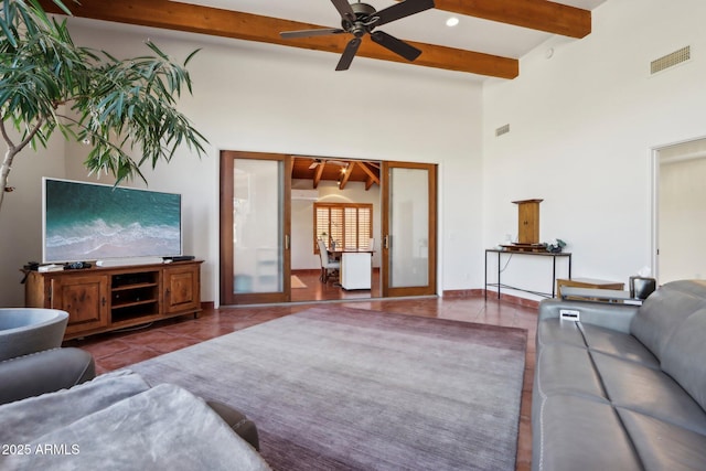 tiled living room featuring ceiling fan, french doors, beamed ceiling, and a high ceiling