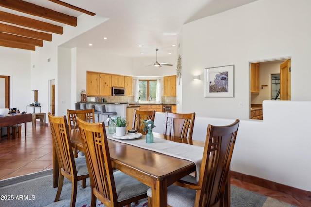 tiled dining space with ceiling fan, a high ceiling, and beamed ceiling