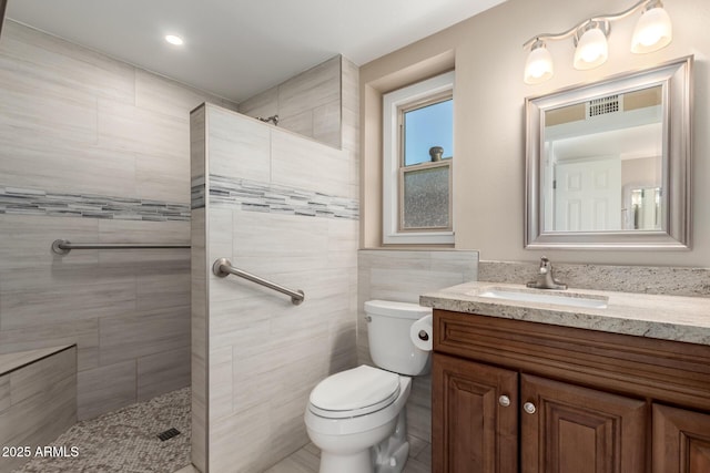 full bath with visible vents, toilet, vanity, a walk in shower, and tile walls