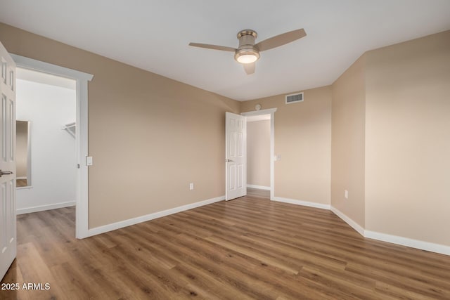 unfurnished room with a ceiling fan, visible vents, baseboards, and wood finished floors