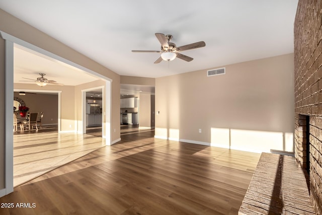 unfurnished living room with a fireplace, visible vents, ceiling fan, wood finished floors, and baseboards