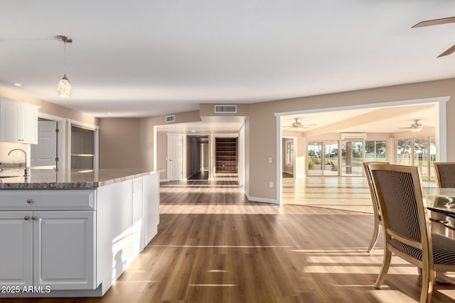 kitchen with visible vents, dark stone counters, wood finished floors, hanging light fixtures, and white cabinetry