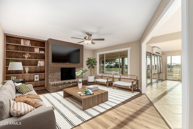 living room with a brick fireplace, a healthy amount of sunlight, an AC wall unit, and wood finished floors