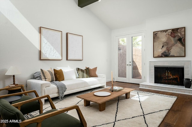 living area featuring lofted ceiling with beams, french doors, a tile fireplace, and wood finished floors