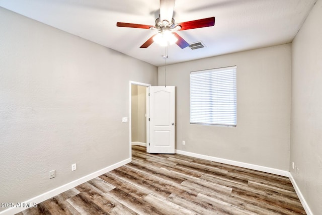 spare room featuring a ceiling fan, visible vents, baseboards, and wood finished floors