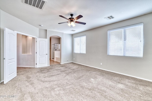 unfurnished bedroom with arched walkways, visible vents, ensuite bath, and carpet flooring