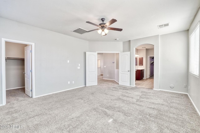 unfurnished bedroom with carpet floors, arched walkways, visible vents, and a spacious closet