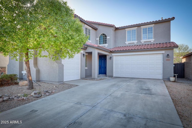 mediterranean / spanish house with an attached garage, driveway, a tile roof, and stucco siding