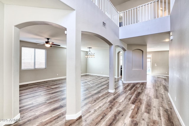 interior space featuring ceiling fan, arched walkways, wood finished floors, visible vents, and baseboards