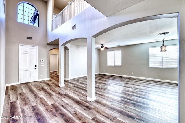 foyer with arched walkways, wood finished floors, visible vents, baseboards, and a ceiling fan