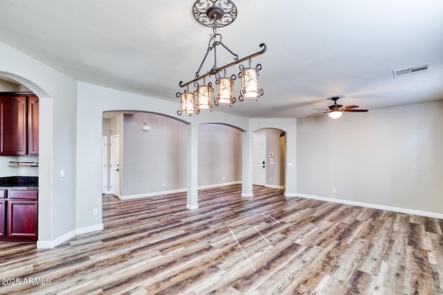 unfurnished dining area with arched walkways, a ceiling fan, baseboards, visible vents, and light wood-style floors