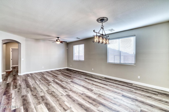 spare room featuring arched walkways, a textured ceiling, wood finished floors, visible vents, and baseboards