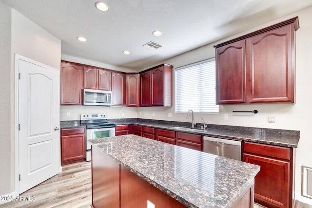 kitchen with reddish brown cabinets, stainless steel appliances, a sink, and visible vents