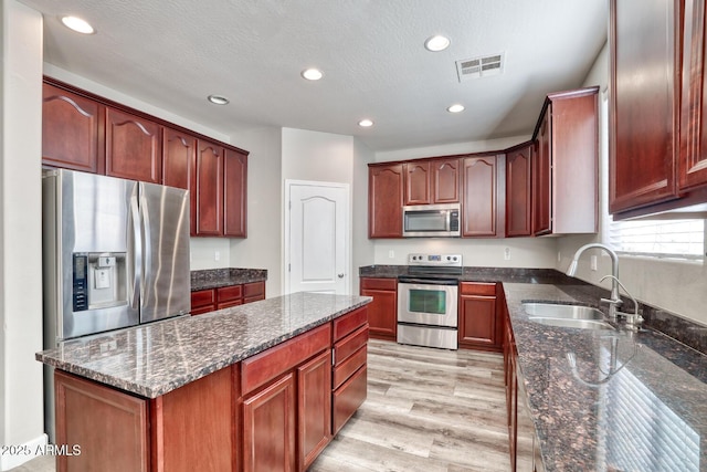 kitchen with visible vents, dark stone counters, light wood-style flooring, appliances with stainless steel finishes, and a sink