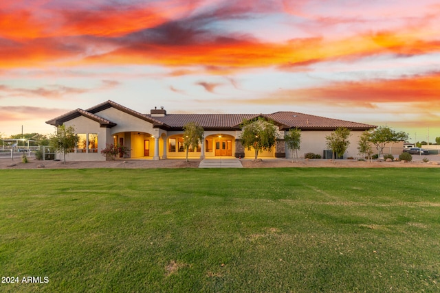 back house at dusk featuring a lawn