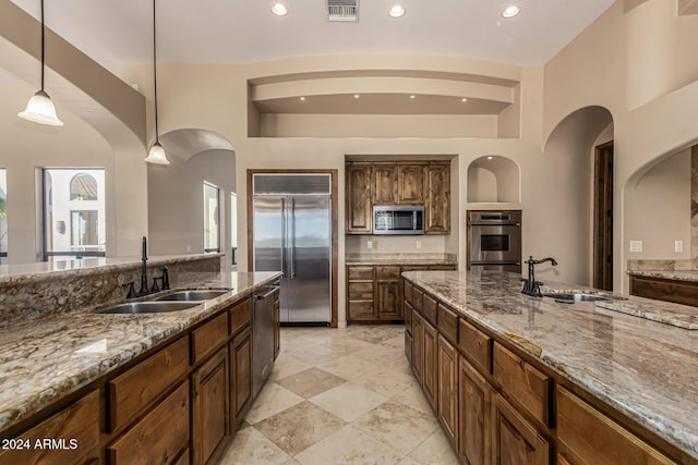 kitchen with appliances with stainless steel finishes, light stone countertops, sink, and pendant lighting