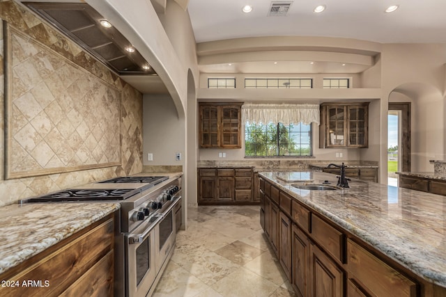 kitchen featuring custom exhaust hood, light stone countertops, sink, and range with two ovens