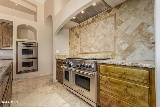 kitchen featuring tile walls, premium range hood, light stone counters, and stainless steel appliances