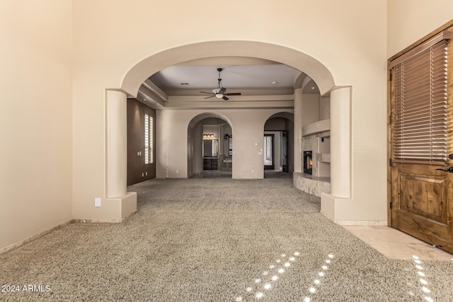 unfurnished living room featuring ceiling fan, a raised ceiling, and carpet flooring