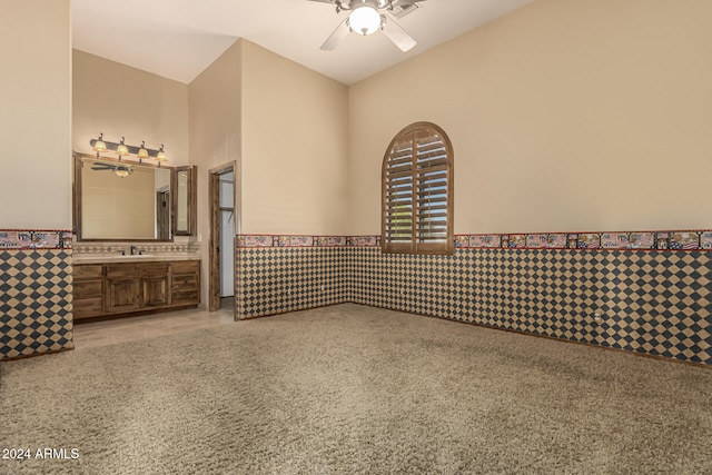 carpeted spare room with ceiling fan, tile walls, and sink