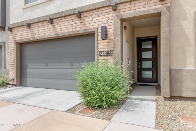 entrance to property featuring stucco siding, driveway, stone siding, and a garage