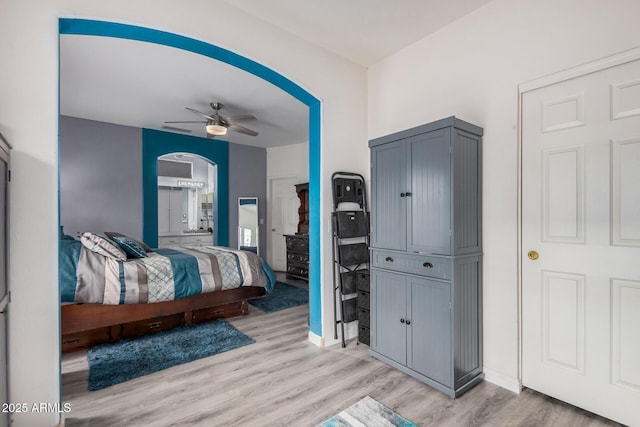 bedroom with ceiling fan, light wood-style floors, arched walkways, and baseboards