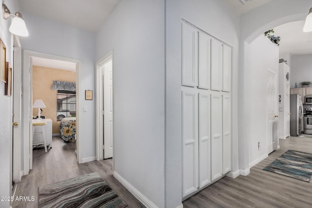 hallway with baseboards, arched walkways, and wood finished floors