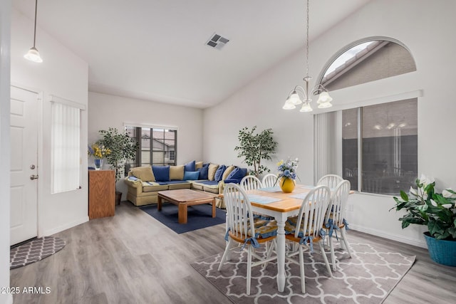 dining space with visible vents, lofted ceiling, wood finished floors, an inviting chandelier, and baseboards