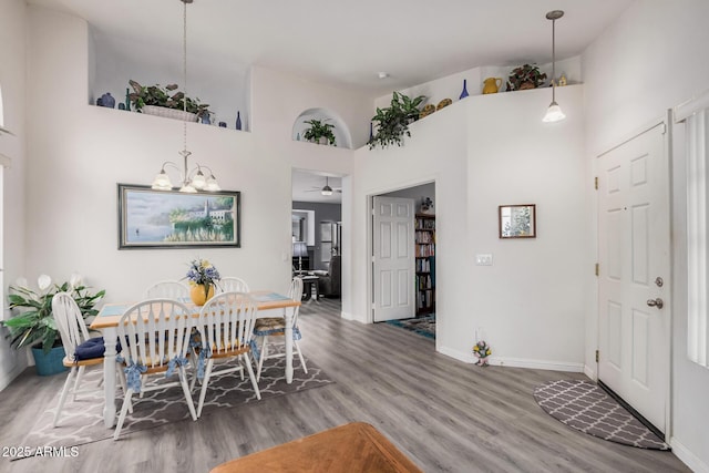 dining room with ceiling fan with notable chandelier, a high ceiling, baseboards, and wood finished floors