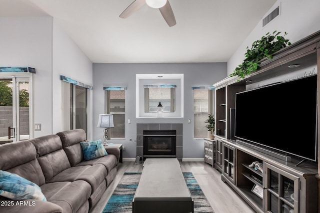 living area with baseboards, visible vents, ceiling fan, light wood-style floors, and a tiled fireplace