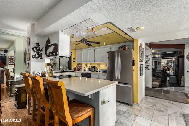 kitchen featuring ceiling fan, a kitchen breakfast bar, kitchen peninsula, stainless steel fridge, and white cabinets