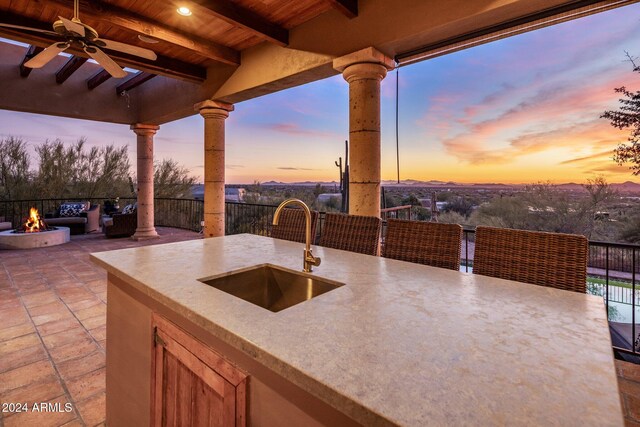 patio terrace at dusk featuring sink, ceiling fan, and an outdoor fire pit