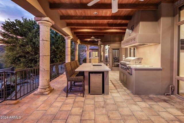 patio terrace at dusk with area for grilling, sink, and ceiling fan