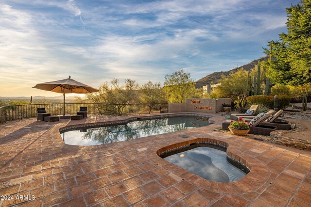 pool at dusk with a patio and an in ground hot tub