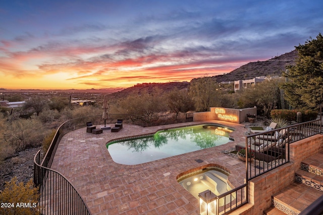 pool at dusk featuring a mountain view, a patio area, and an in ground hot tub