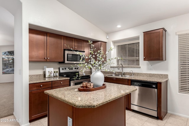 kitchen with light stone counters, a kitchen island, lofted ceiling, a sink, and stainless steel appliances