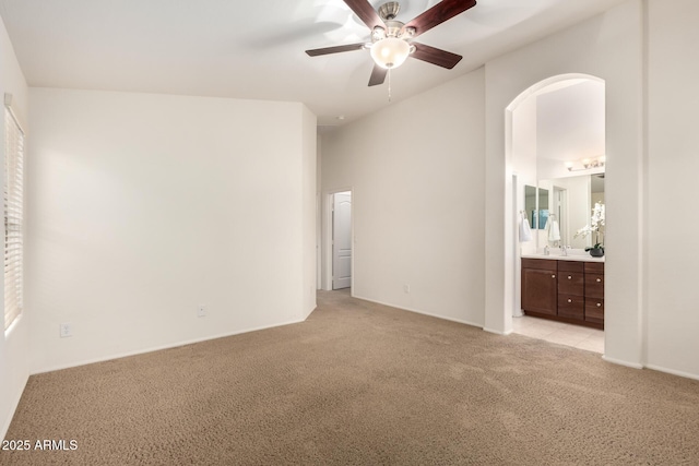 unfurnished bedroom with a ceiling fan, arched walkways, a sink, ensuite bathroom, and light carpet