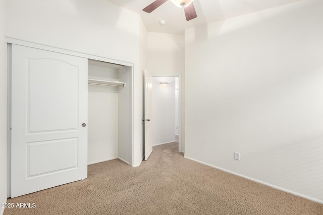 unfurnished bedroom with a closet, light colored carpet, baseboards, and ceiling fan