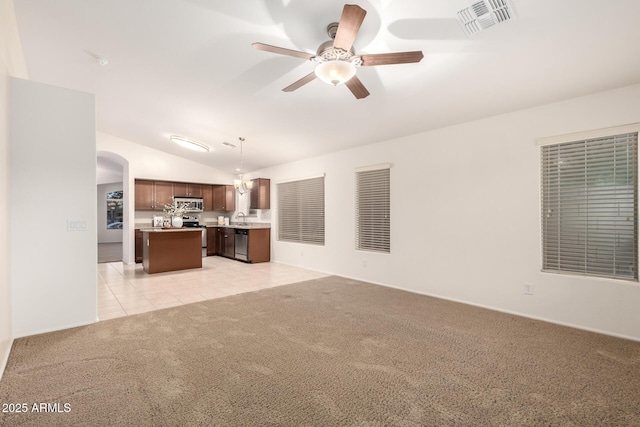 unfurnished living room featuring ceiling fan, light colored carpet, vaulted ceiling, light tile patterned flooring, and arched walkways