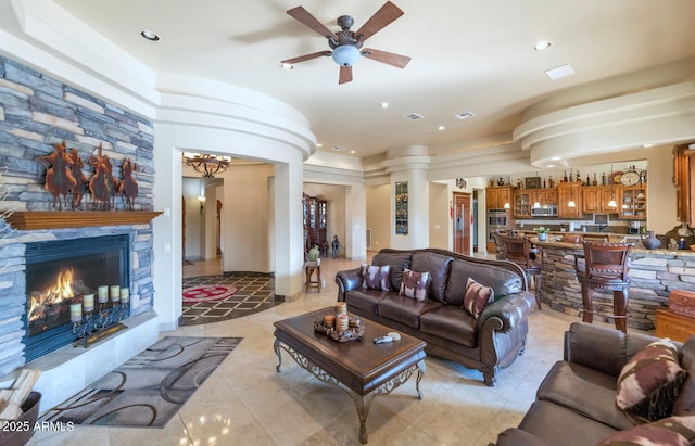 tiled living room featuring ceiling fan, a stone fireplace, and decorative columns