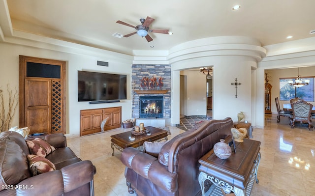 living room featuring ceiling fan with notable chandelier and a stone fireplace