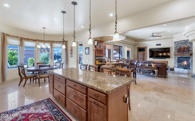 kitchen featuring a fireplace, light stone countertops, pendant lighting, ceiling fan with notable chandelier, and a center island