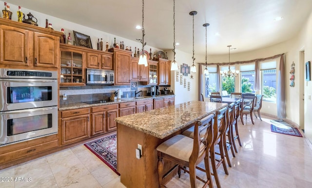 kitchen with pendant lighting, a kitchen island, a breakfast bar, light stone countertops, and appliances with stainless steel finishes