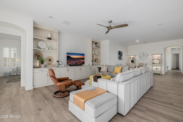 living room with built in features, ceiling fan, and light wood-type flooring