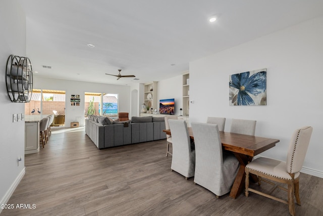 dining room with wood-type flooring, built in features, and ceiling fan