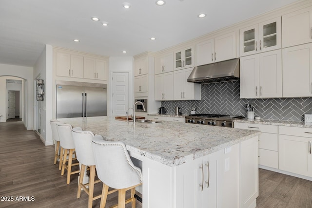 kitchen featuring light stone counters, stainless steel built in refrigerator, sink, and an island with sink