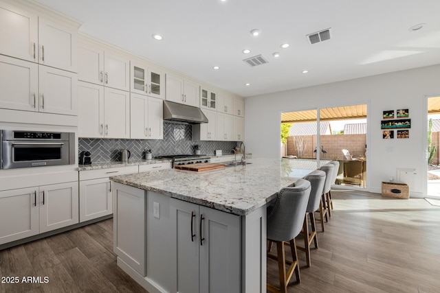 kitchen featuring light stone counters, white cabinets, an island with sink, and stainless steel oven