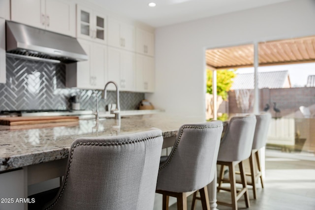 kitchen with white cabinetry, sink, backsplash, and light stone counters