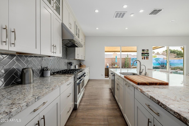 kitchen with sink, white cabinetry, appliances with stainless steel finishes, light stone countertops, and backsplash